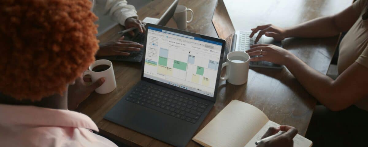 Three people in a meeting at a table discussing schedule on their Microsoft laptop